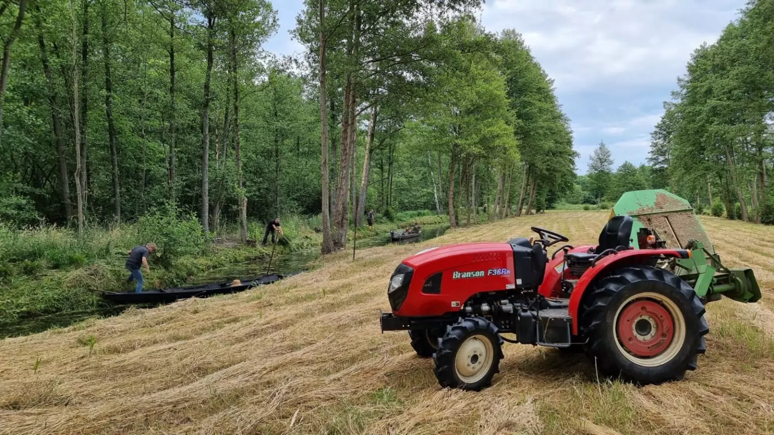 Lehdscher schneiden das Ufergras und auf der Wiese steht ein Traktor.